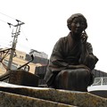 写真: 林芙美子像 in 尾道駅前　芙美子の左後ろに小さく見えるのは国際観光旅館の千光寺山荘。この日は悲しいことに、PM2.5の濁った空が広がっていた。